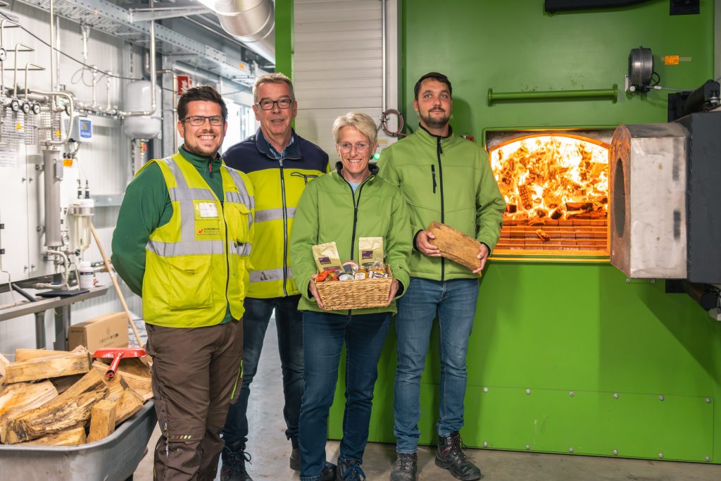 Mitarbeiter vor dem Ofen, der eingeheizt wurde. Mit Holzstück und Geschenkkorb in der Hand.