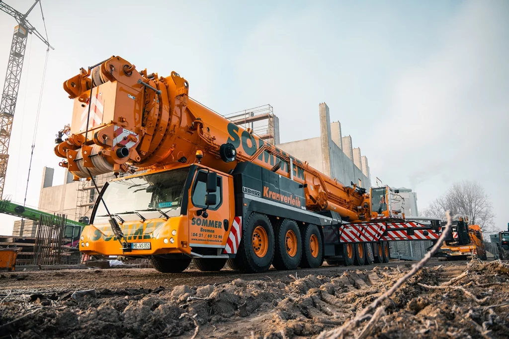 Ein orangener 700-Tonnen schwerer Kran steht vor einer Biomasseanlage. Der Boden ist matschig.