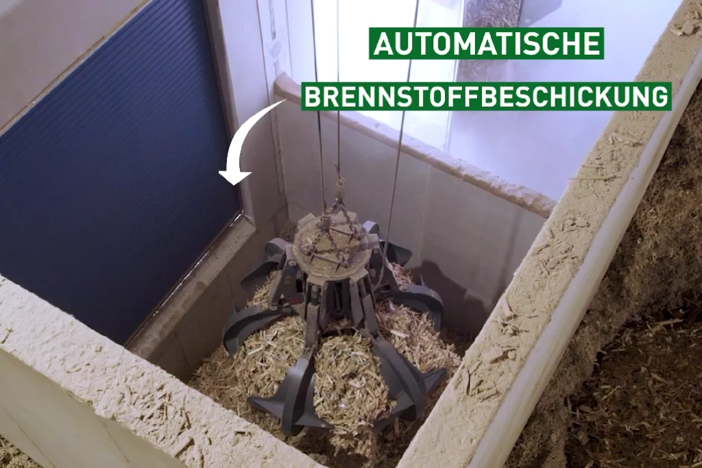 Ein Greifarm mit einer Ladung Holzhackschnitzel in einem Schacht zeigt die automatische Brennstoffbestickung
