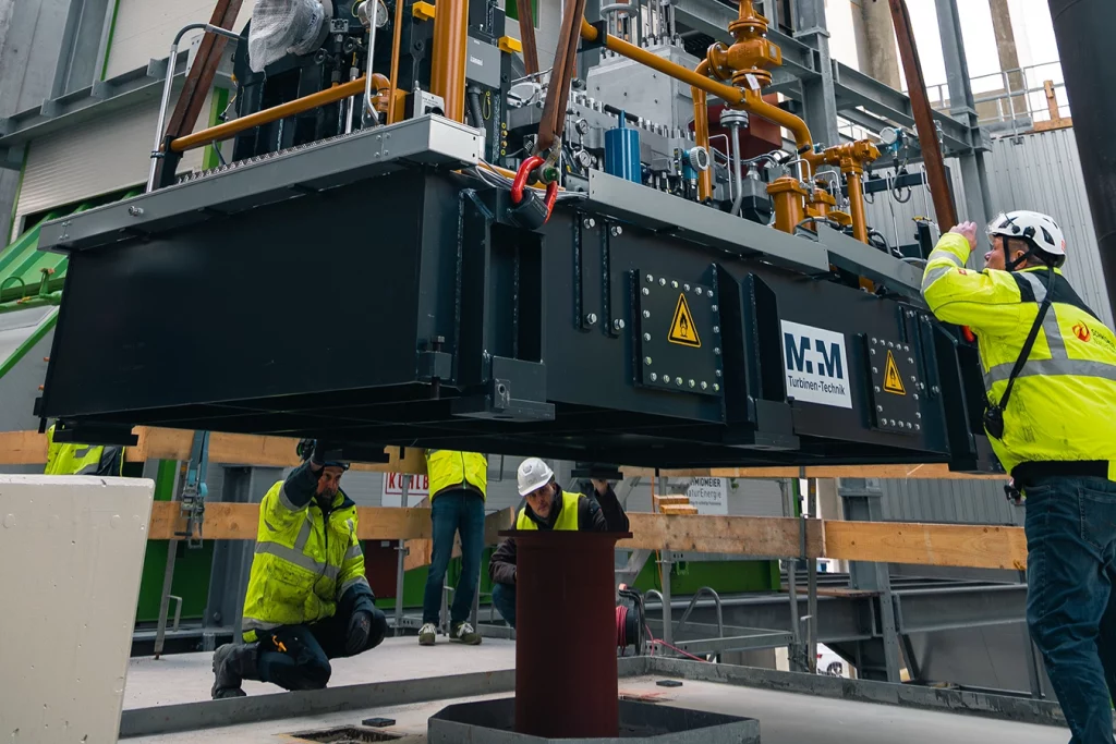 Mitarbeiter von Schmidmeier NaturEnergie unterstützen den Kran beim Einsetzen einer Turbine in einer Biomasseanlage in Bremen. Die Mitarbeiter tragen eine gelbe Sicherheitsweste.
