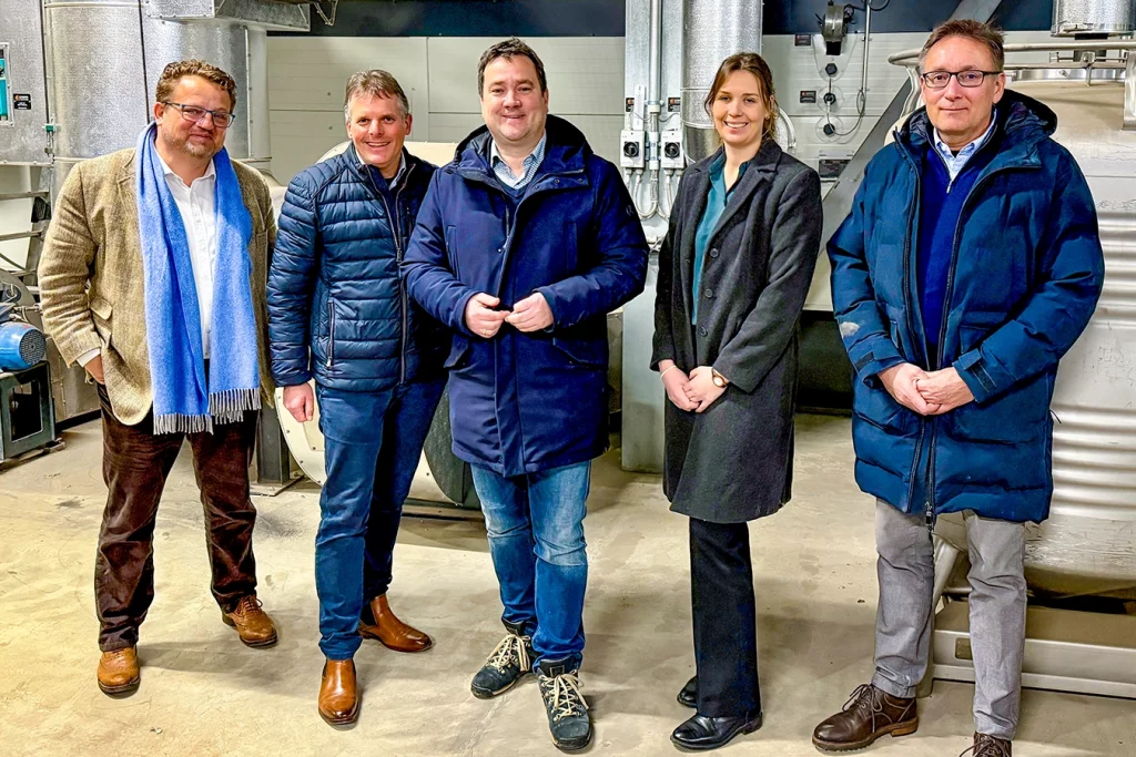 Gruppenfoto bestehend aus Thomas Schmidmeier (Geschäftsführer von Schmidmeier NaturEnergie), Anna Marlen Vöcking, Pete Heuer und zwei Personen aus der Politik. Sie stehen in einer Biomasseanlage.