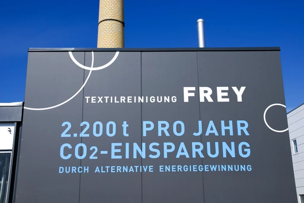 Holzpellet-Dampfkessel in Burgau. Die Anlage ist schwarz mit blauer Aufschrift "2.200t pro Jahr CO2-Einsparung durch alternative Energiegewinnung".