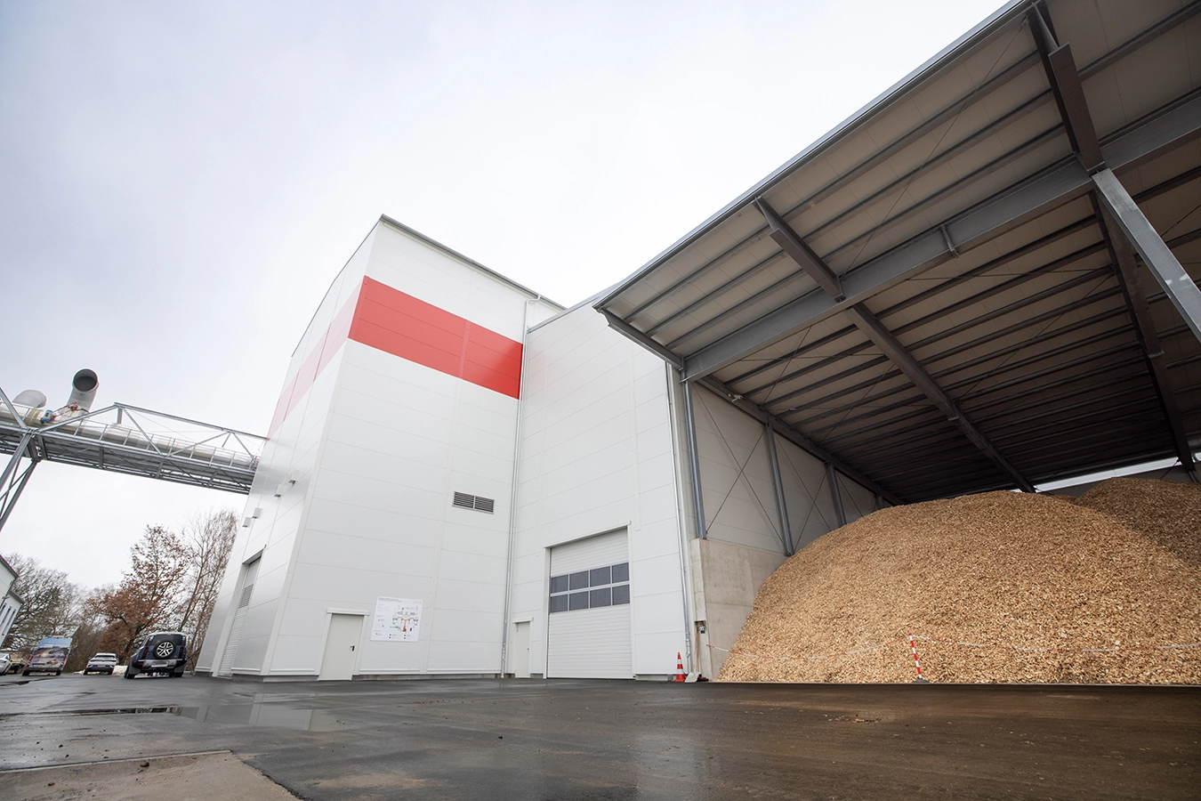 Biomasse-Heißgas-Anlage in Freihung. Rechts an der Anlage schließt ein überdachtes Brennstofflager mit Holzhackschnitzel an. Die Anlage ist weiß-grau mit einer roten Sequenz.