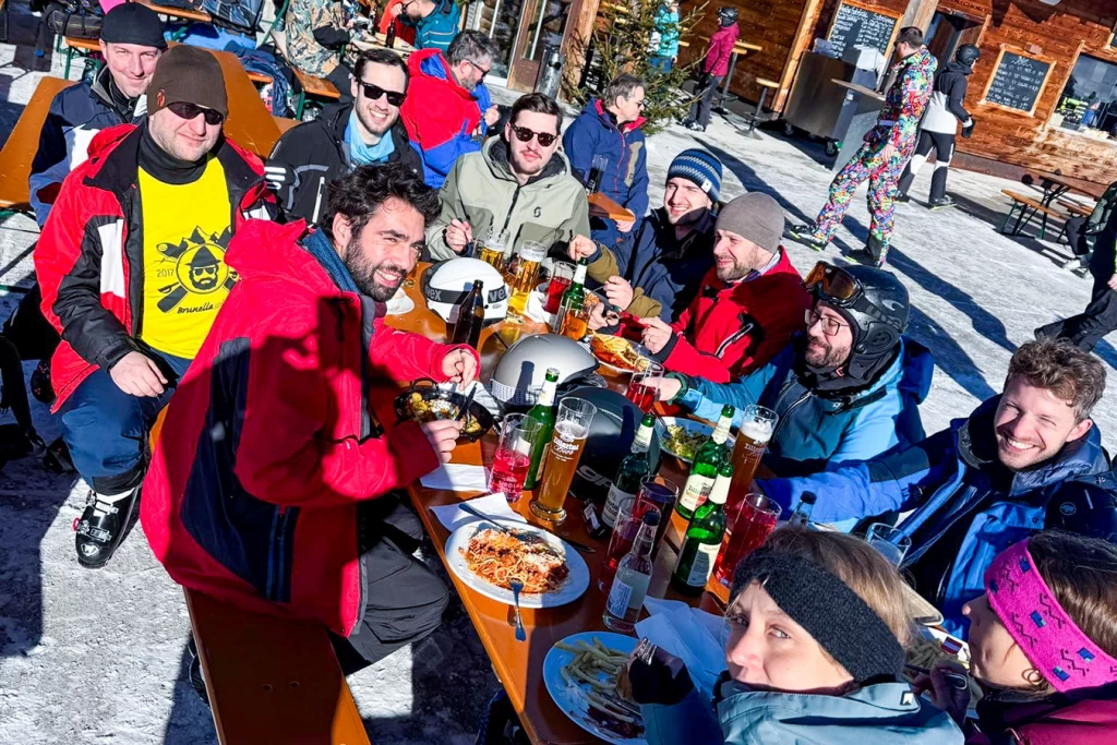 Mitarbeiter und Mitarbeiterinnen von Schmidmeier NaturEnergie GmbH sitzen gemeinsam an einem Tisch einer Berghütte und genießen ihr Essen und Trinken.