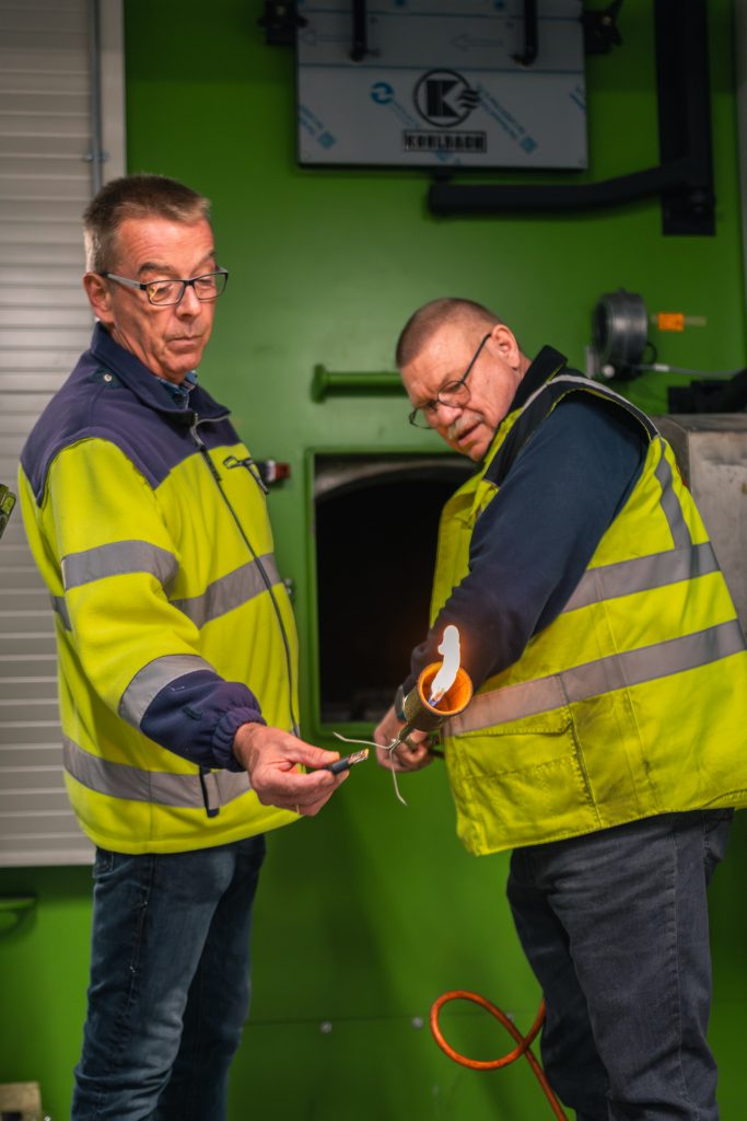 Zwei Mitarbeiter beginnen mit dem Einheiz-Prozess. Und machen Feuer mit einem Feuerzeug.