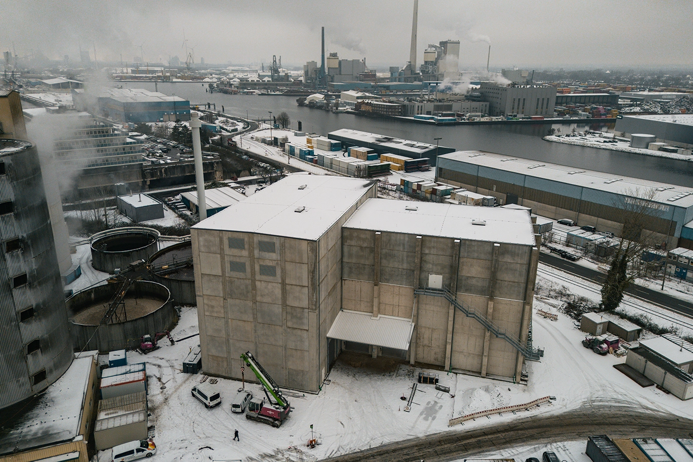 Drohnenaufnahme von einer Biomasseanlage am Bremer Hafen. Das Dach der Biomasse ist mit Schnee bedeckt. Hinter der Anlage fließt die Weser vorbei.