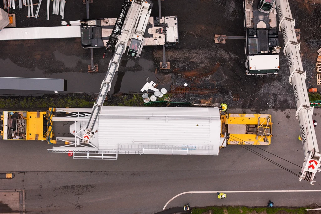 Aus der Vogelperspektive sieht man einen langen gelben LKW der ein Silo transportiert. Ein Silo ist ein großer Speicher für Schuttgüter, in diesem Fall der Biomasse.