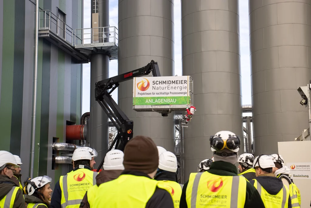 Mitarbeiter der Schmidmeier NaturEnergie bei der Besichtigung einer Anlage. Man sieht sie nur von hinten und sie tragen Schutzhelme und Warnwesten.