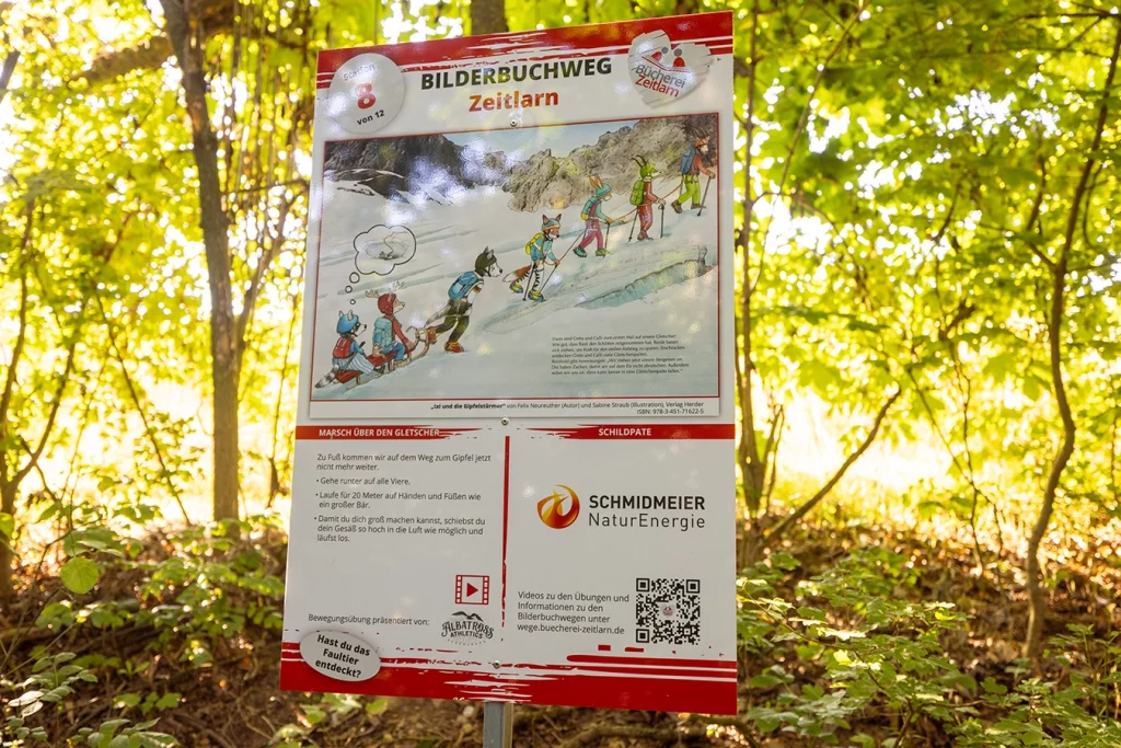 Zu sehen ist ein Schild, welches im Wald angebracht ist. Es gehört zu dem Bilderbuchweg in Zeitlarn. Auf dem Schild gibt es ein Bild sehen mit einem zusammenhängenden Text. welcher beschreibt, was man an dieser Station machen muss. Das Logo von der Schmidmeier ist auf dem Schild platziert, da sie der Schildpate ist.