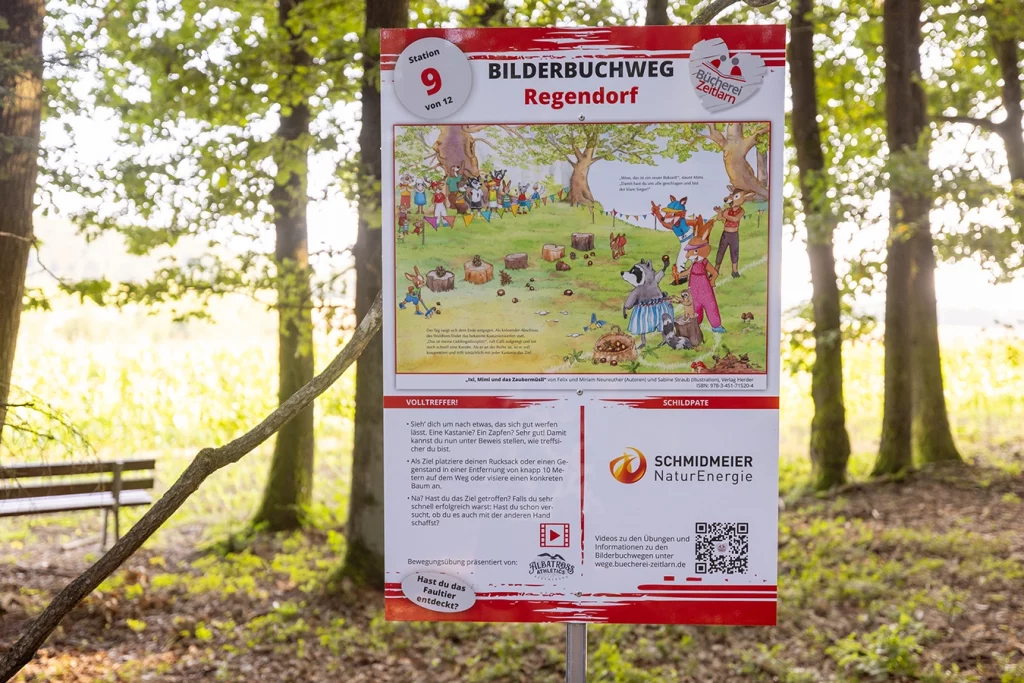 Zu sehen ist ein Schild, welches im Wald angebracht ist. Es gehört zu dem Bilderbuchweg in Zeitlarn. Auf dem Schild gibt es ein Bild sehen mit einem zusammenhängenden Text. welcher beschreibt, was man an dieser Station machen muss. Das Logo von der Schmidmeier ist auf dem Schild platziert, da sie der Schildpate ist.