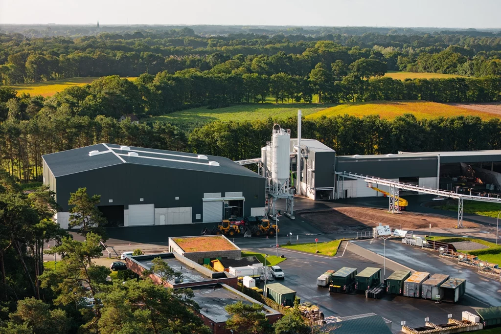 Inmitten einer grünen Landschaft von Bäumen liegt ein kleines Industriegelände mit Biomassekessel und einer Biogasaufbereitungsanlage