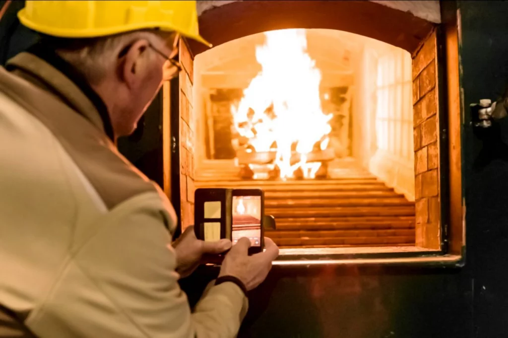 Feuer im Feuerraum des Biomasseheizwerks brennt. Mitarbeiter der Firma Steinicke fotografiert das Feuer mit seinem Handy.