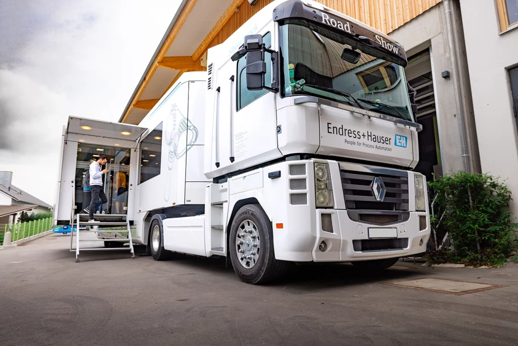 Ein weißer LKW mit der Aufschrift "Endress + Hauser" steht auf dem Hof des Firmengeländes der Schmidmeier NaturEnergie. Auf der linke Seite frontal betrachtet, hat dieser einen zusätzlichen Raum ausgefahren, der über eine Treppe begehbar ist.