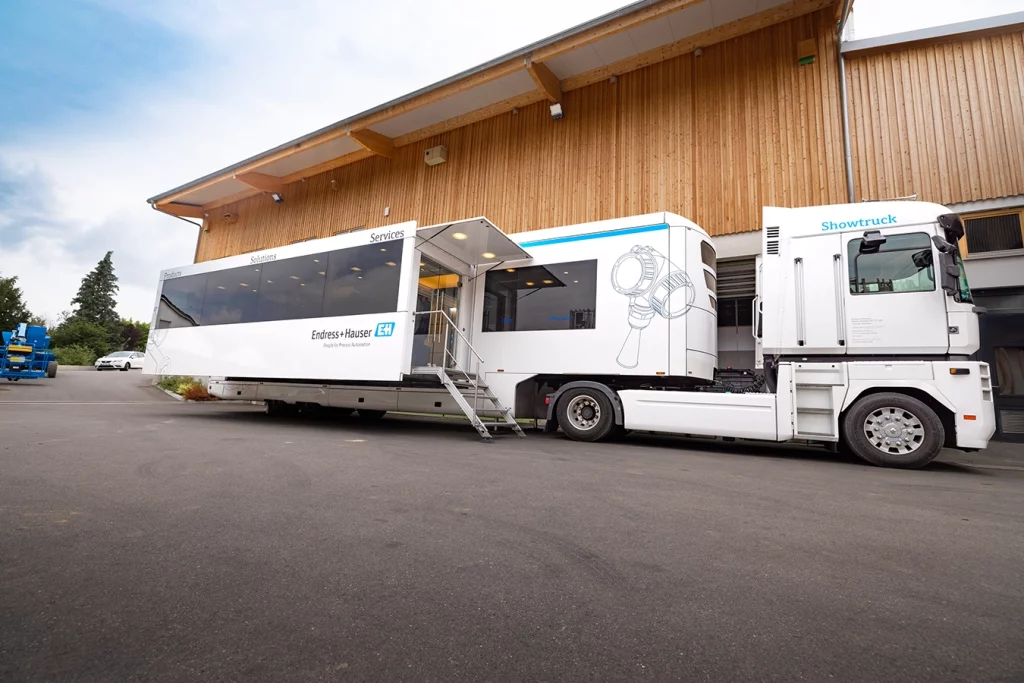 Ein weißer LKW mit der Aufschrift "Endress + Hauser" steht auf dem Hof des Firmengeländes der Schmidmeier NaturEnergie. Auf der linke Seite frontal betrachtet, hat dieser einen zusätzlichen Raum ausgefahren, der über eine Treppe begehbar ist.