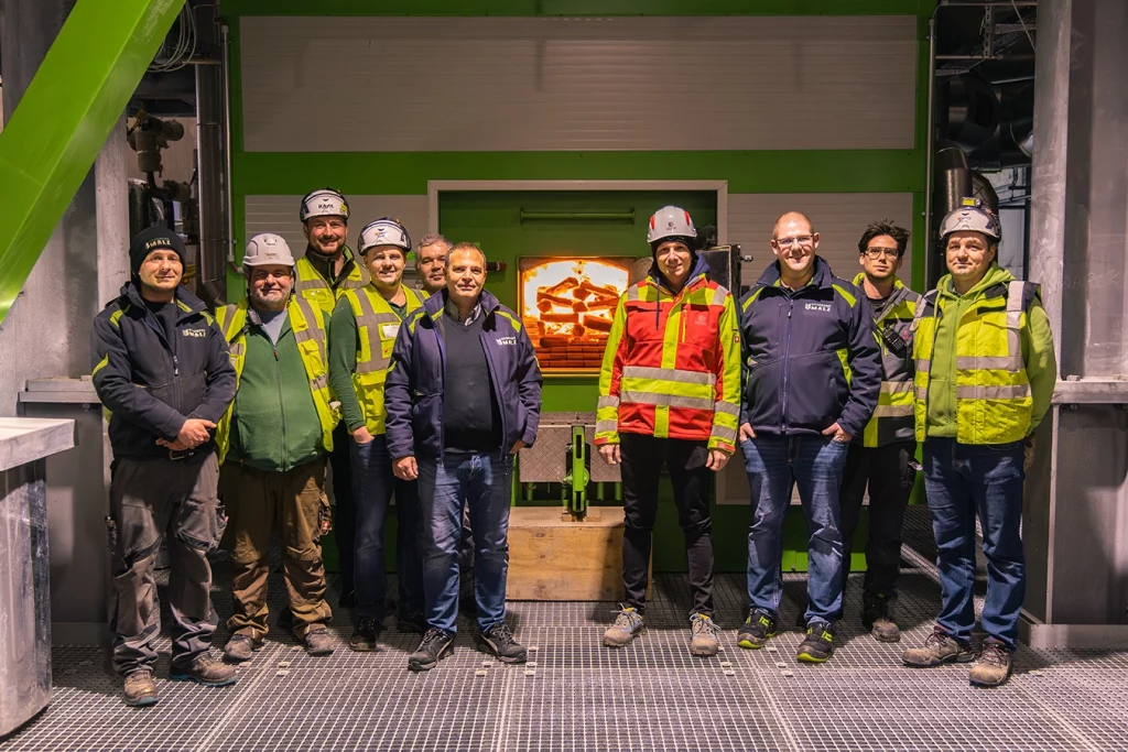 Eine Gruppe an Männern steht vor einem Kessel einer Biomasseanlage in Bremen. Zentral im Hintergrund ist der offene und brennende Kessel zu sehen.