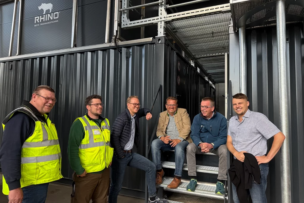 Ein Gruppenbild aus sechs Personen vor schwarzen Containern. Zwei Personen sitzen auf einer kleinen Treppe zwischen zwei Containern. Die linke Person davon ist Geschäftsführer Thomas Schmidmeier, neben ihm stehend befindet sich sein Sohn Ferdinand Schmidmeier, auch Geschäftsführer. Neben dem zweiten sitzenden steht der Mitarbeiter Dominik Bauer. Neben Florian Schmidmeier steht der Mitarbeiter in neongelber Warnweste Martin Goldbach.