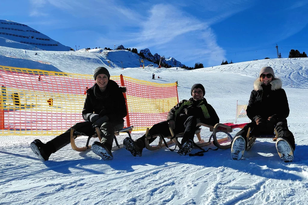 Gruppenbild von drei Mitarbeiten der Schmidmeier NaturEnergie. Sie sitzen alle auf einem Schlitten im Schnee.