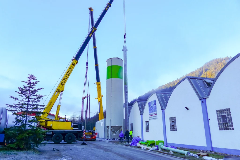 Baustelle einer Biomasse-Dampfanlage. Rechts im Bild steht das längliche Gebäude der Wäscherei Kafa. Neben diesem Gebäude wird die Biomasse-Dampfanlage gebaut. Ein gelber Kran hebt einen Kamin.
