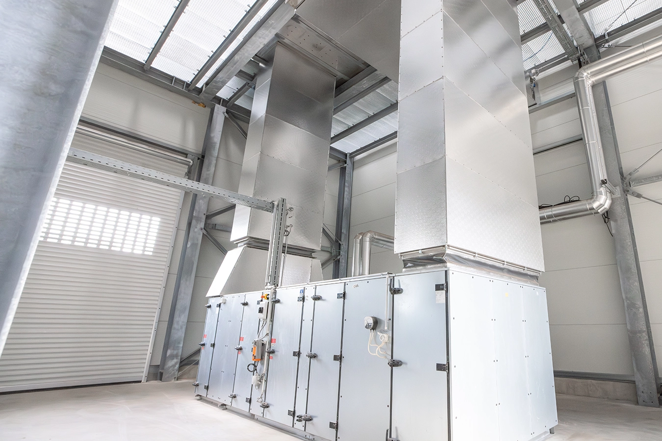 Biomasse-Heißgas-Anlage in Freihung von innen. Eine Komponente aus Metall hat zwei rechteckige Rohre, die bis zur Decke führen.