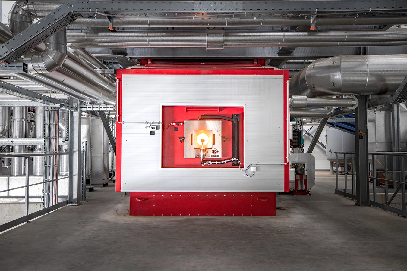 Biomasse-Heißgas-Anlage in Freihung von innen. Ein Kessel mit rotem Rahmen liegt in der Mitte. Drum herum an den Wänden und der Decke befinden sich Rohre aus Metall.