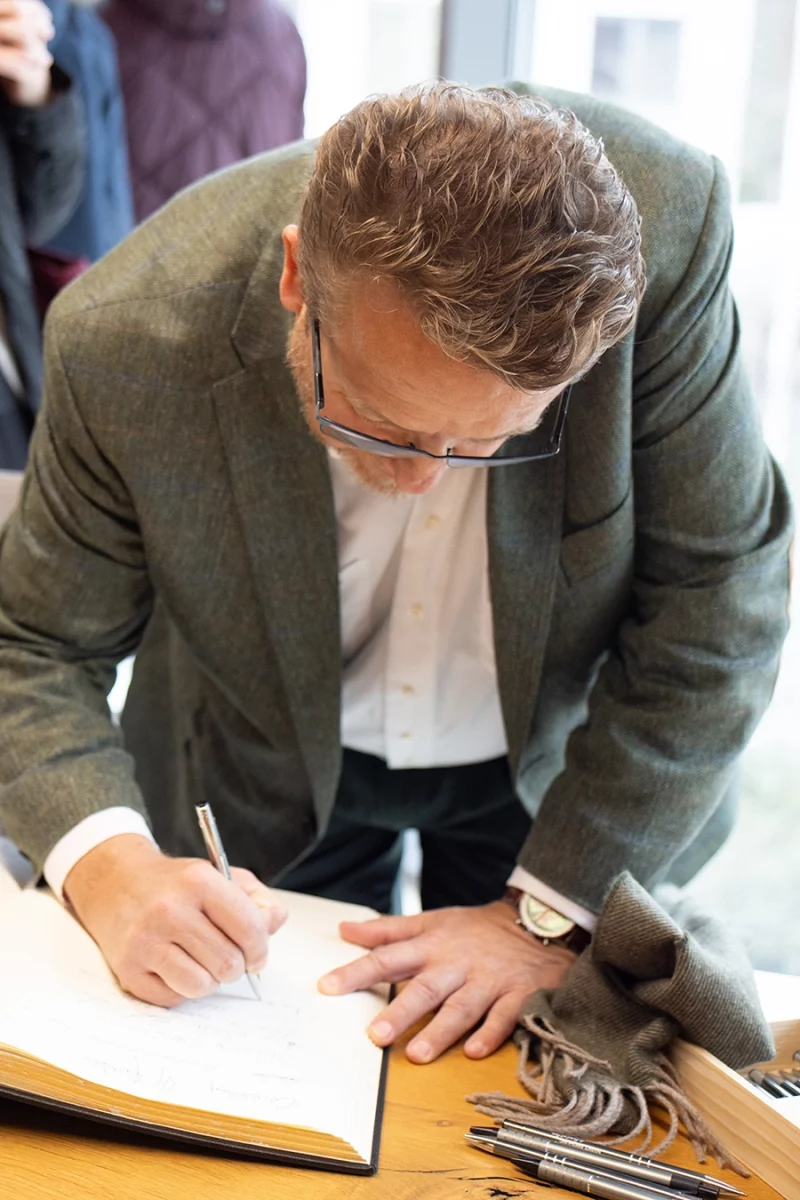 Thomas Schmidmeier, Geschäftsführer der Schmidmeier NaturEnergie, unterschreibt einem Buch. Er trägt eine grünes Jackett.