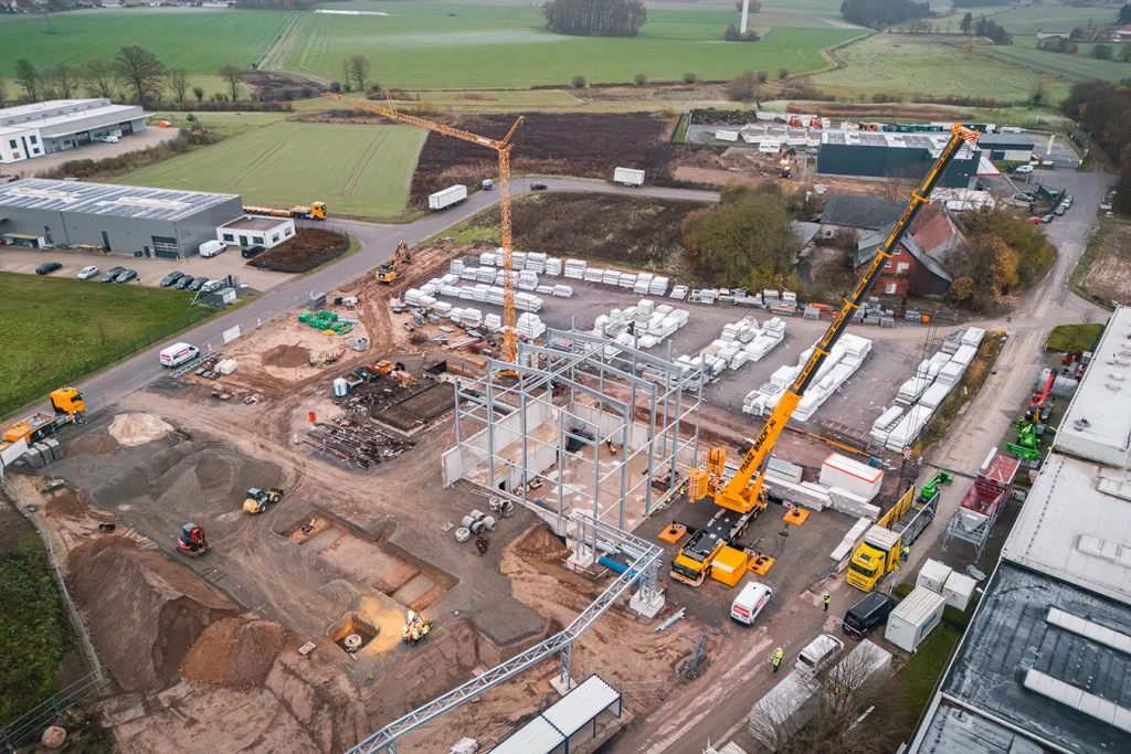 Baustelle einer Biomasseanlage aus der Vogelperspektive. Das Grundgesteht des Gebäudes steht bereits, zudem sieht man zwei orangefarbene Kräne.
