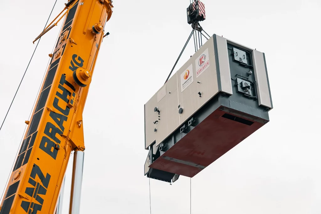 Ein orangener Kran transportiert eine Komponente einer Biomasseanlage.