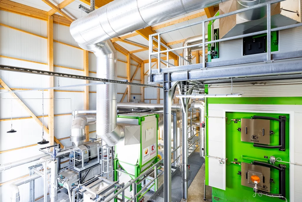 Biomasseanlage in Kirchheim von innen. Verschiedene graue Rohrleitungen und Komponenten wie der Heizkessel sind zu sehen.