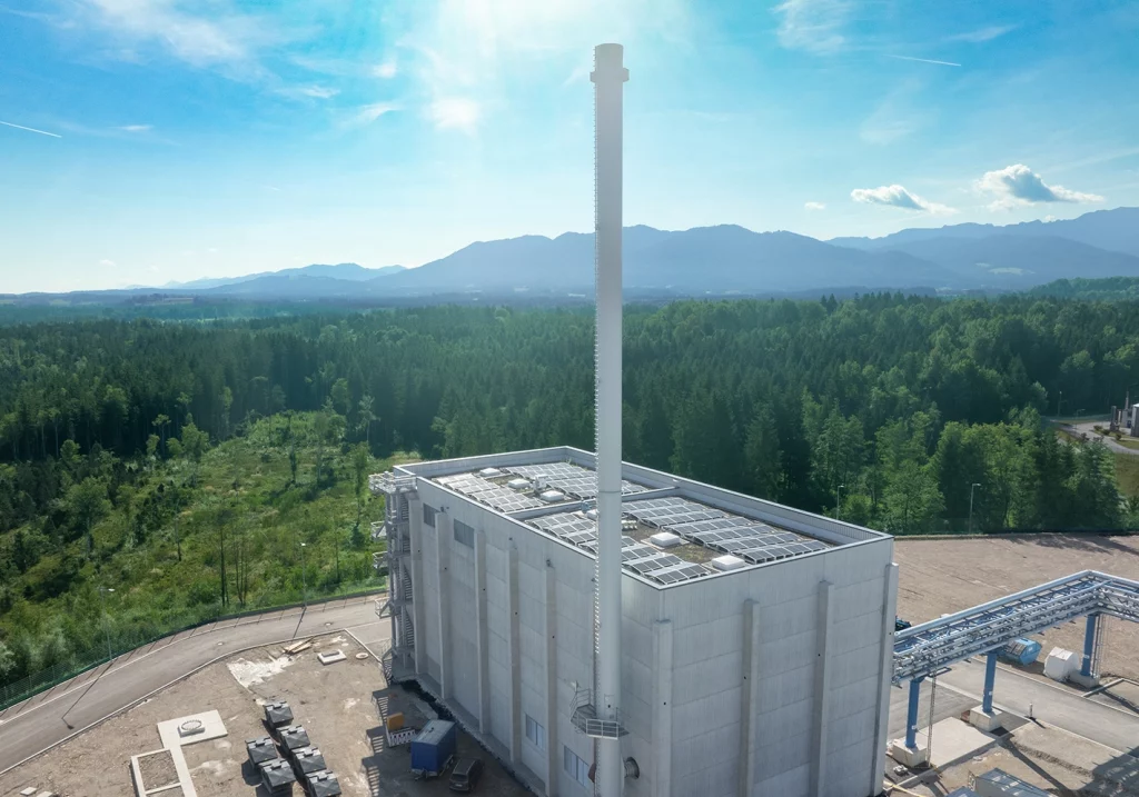 Drohnenaufnahme der Biomasse Anlage in Penzberg. Es scheint die Sonne und hinter dem Gebäude sieht man einen Nadelwald.