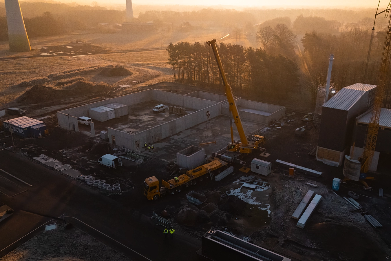 Baustelle eines Biomassekessels während die Sonne tief steht. Der Grundriss eines Gebäudes und zwei Kräne sind zu sehen.