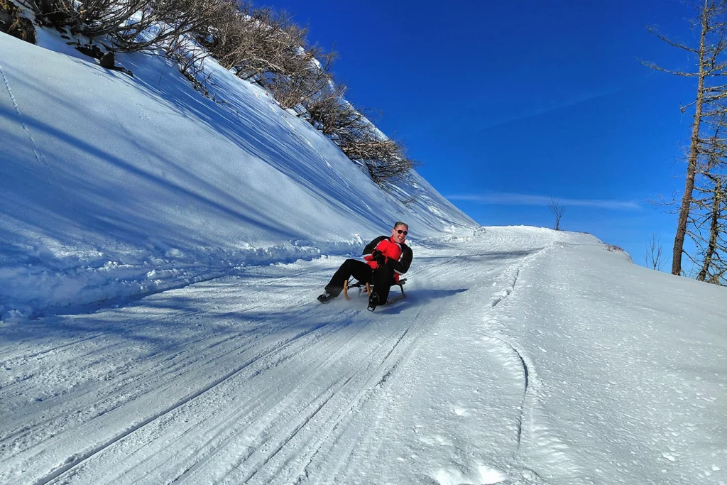 Ein Mitarbeiter der Schmidmeier NaturEnergie fährt lachend den Berg auf einem Schlitten hinunter.