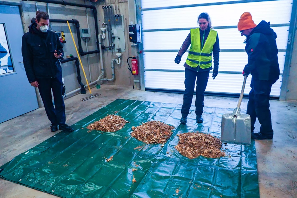 Drei Mitarbeiter der Technologica machen eine Probe von Altholz. Dafür liegen drei kleine Häufchen Altholz auf einer grünen Plane und werden analysiert.