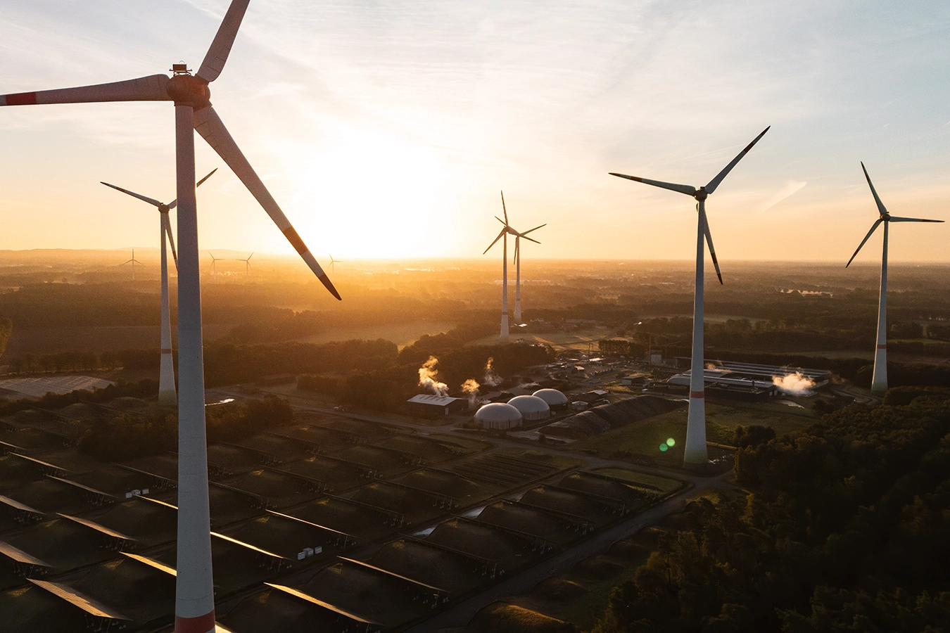 Eine Drohnenaufnahme zeigt Windräder und PV-Anlagen in Steinfurt während die Sonne im Hintergrund untergeht