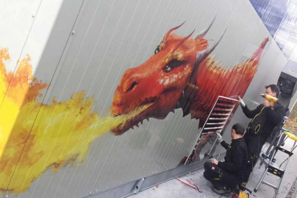 Zeichnung eines roten, feuerspuckenden Drachens an einer Wand und zwei Arbeiter