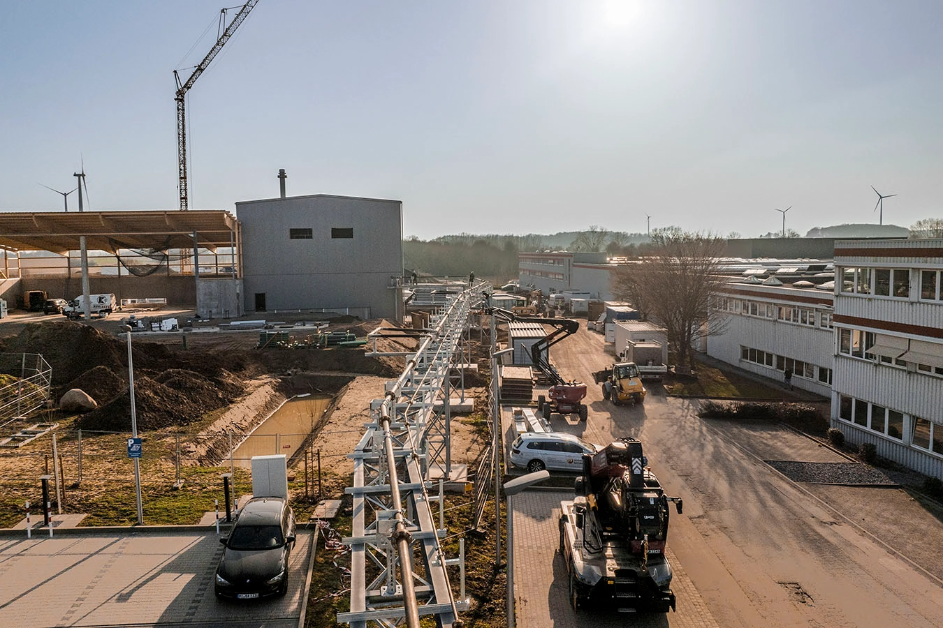 Eine Rohrbrücke führt zu einer Biomasseanlage in Hüllhorst. Rechts neben der Brücke stehen drei Bagger. Links davon erstreckt die gesamte Baustelle mit aufgehäufter Erde.