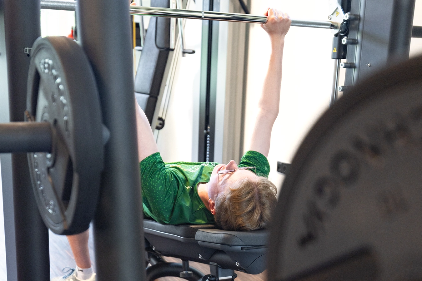 Ein Mitarbeiter stemmt liegenderweise im grünen Firmentrikot Gewichte