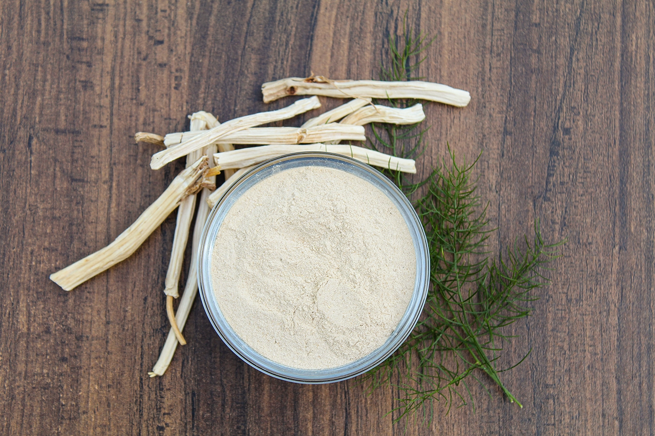 Shatavari‑Pulver in einer Schale mit Wurzeln auf Holzuntergrund, Sicht von oben
