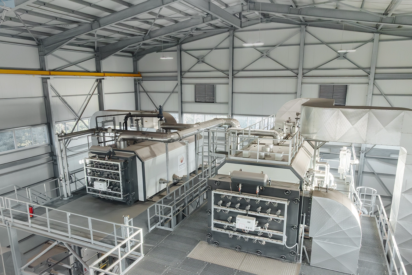 Inneneinrichtung einer Biomasseanlage. In einer großen grauen Halle stehen mittig zwei Komponenten, die mit Rohren verbunden sind.