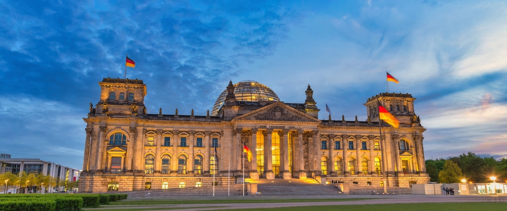 Frontansicht des deutschen Bundestages bei Dämmerung vor dunklem Himmel, das Gebäude ist beleuchtet