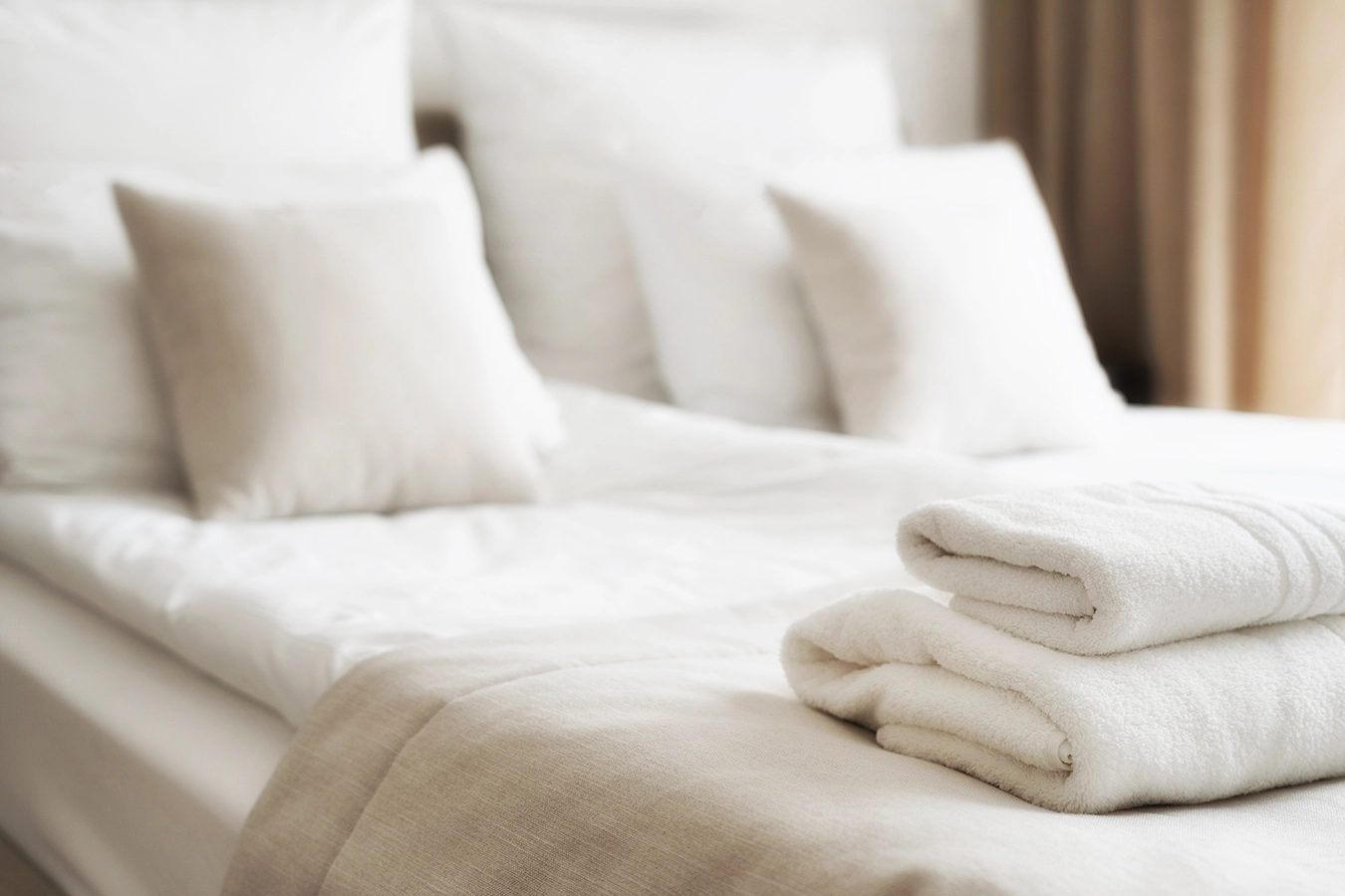 Aufnahme eines Hotelbettes mit weißen Bettlacken und frischen weißen Handtüchern.