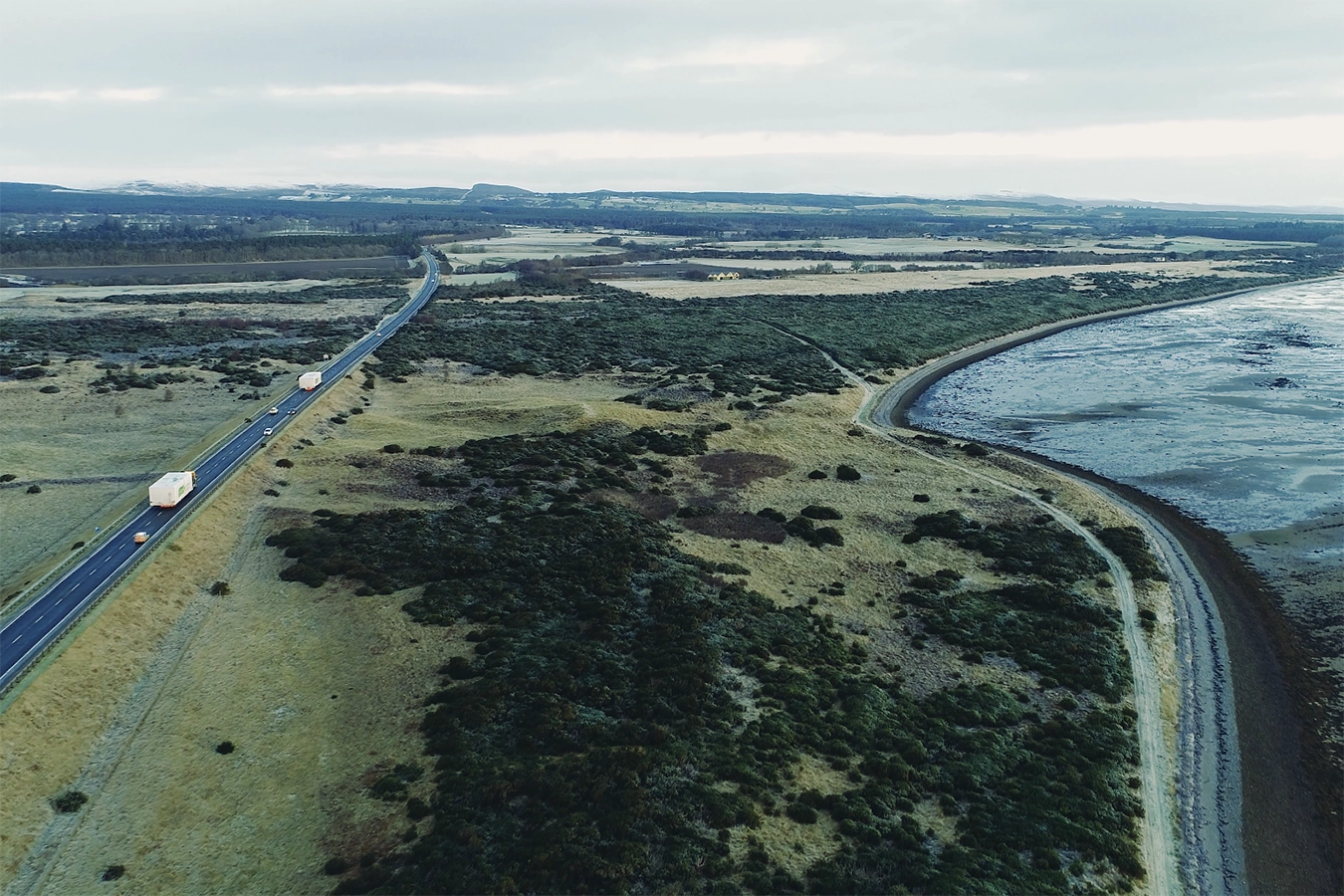 Ansicht von oben: Prozess der Anlieferung mit großen Transportwägen auf der Straße und idyllischer Landschaft im Hintergrund.