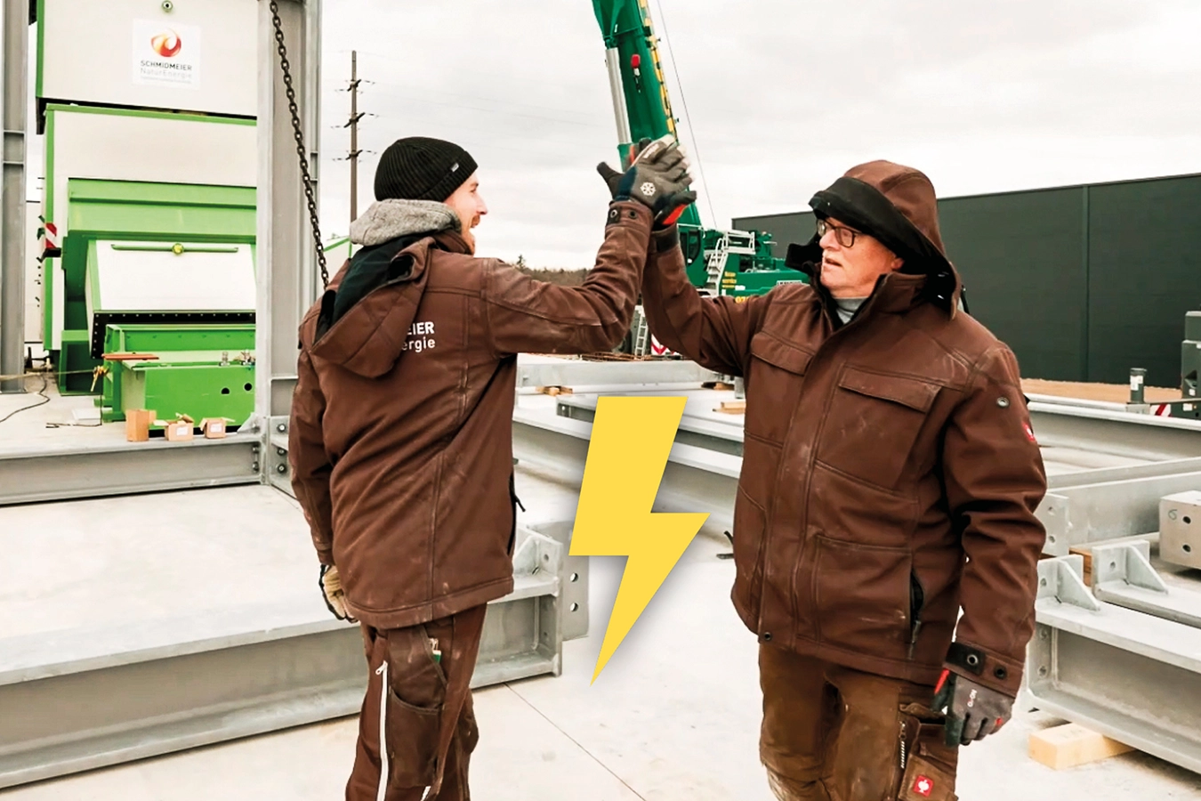 Zwei Mitarbeiter der Schmidmeier NaturEnergie klatschen auf der Baustelle ab. Ein Blitz-Symbol zeigt an, dass es sich um eine Stellenausschreibung für Elektriker handelt